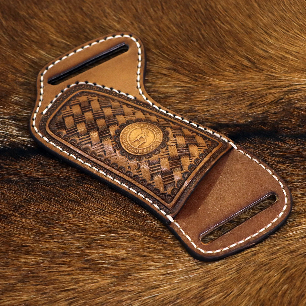 A handcrafted brown leather knife sheath with a decorative pattern and a belt loop resting on a brown fur background.