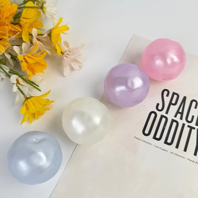 A collection of translucent, spherical fidget balls in shades of yellow, pink, purple, and white resting on a white surface.