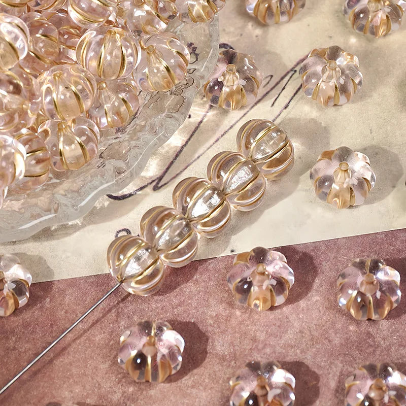 A collection of small, gold-traced pumpkin resin beads for jewelry making scattered on a surface.