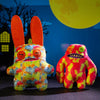 A colorful, fuzzy monster plush doll with large teeth is displayed against a blue background with a yellow moon.