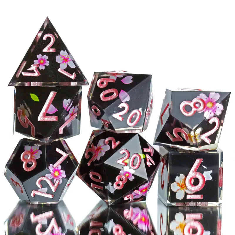 A set of black and pink resin polyhedral dice with floral designs shown from an angle.