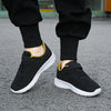 A pair of black mesh sneakers with yellow accents worn by a person, viewed from the side.