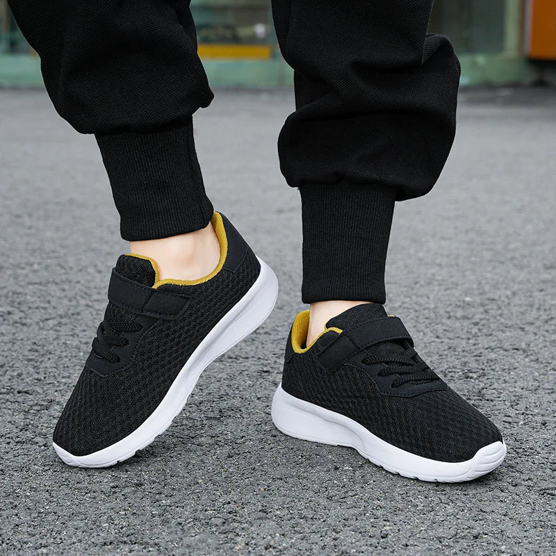 A pair of black mesh sneakers with yellow accents worn by a person, viewed from the side.