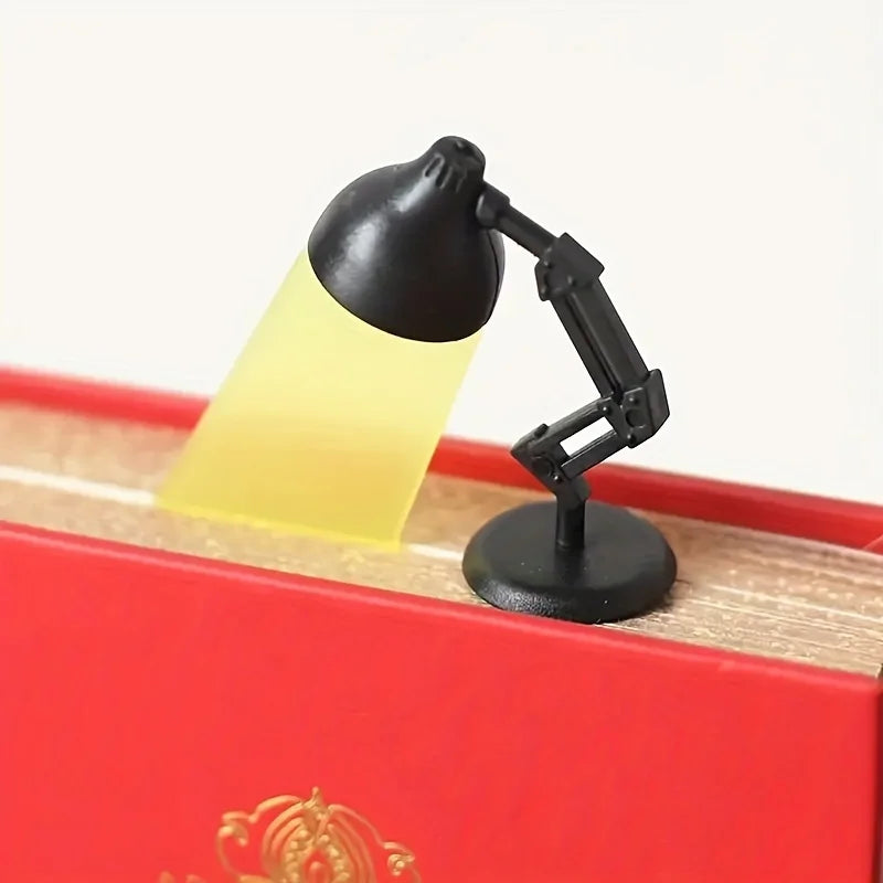 A black cartoon desk lamp bookmark with a yellow light shines onto a wooden surface inside a red box.
