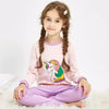 A young girl wearing a pink long-sleeved top and purple pants with an astronaut print, sitting on a white fluffy surface.
