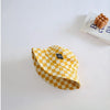 A yellow and white checkerboard bucket hat is shown on a white surface next to a book.