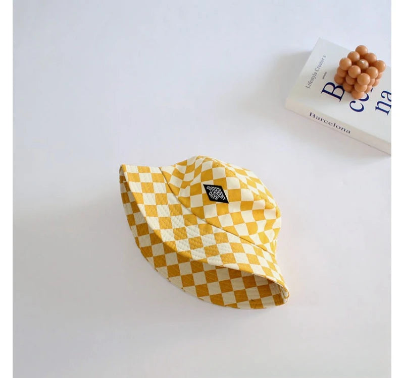 A yellow and white checkerboard bucket hat is shown on a white surface next to a book.