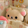 A soft plush Rilakkuma hand rest pillow with pink ears resting on a white bed.