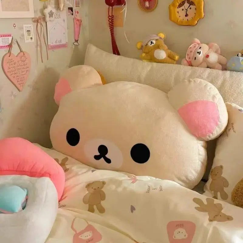A soft plush Rilakkuma hand rest pillow with pink ears resting on a white bed.