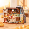 A miniature dollhouse kit depicting a cozy baking kitchen with wooden cabinets and tools.