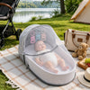 A portable foldable baby bed with a mosquito net and mattress is set up outdoors on a blanket.