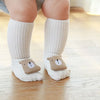 A pair of white cotton socks with brown cartoon animal feet are worn by a baby or toddler.