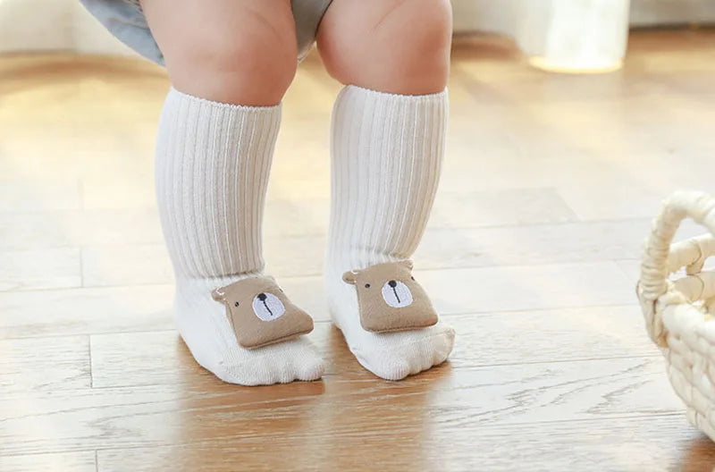 A pair of white cotton socks with brown cartoon animal feet are worn by a baby or toddler.