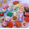 A collection of miniature dollhouse-themed snack foods including cookies, cakes, and candies arranged on a white surface.