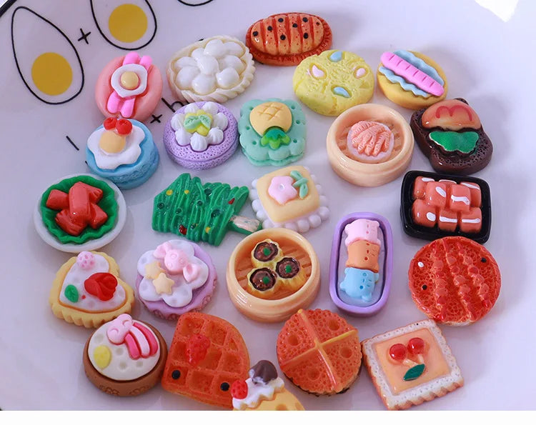 A collection of miniature dollhouse-themed snack foods including cookies, cakes, and candies arranged on a white surface.