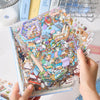 A hand holds an open sticker book featuring colorful 3D miniature scene decor stickers.