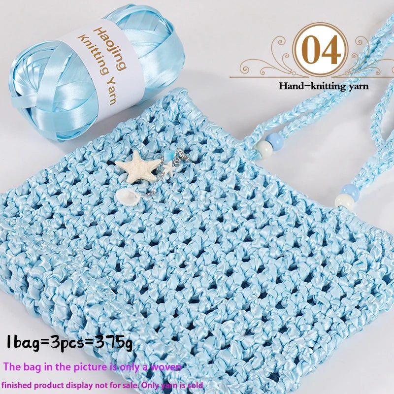 A light blue crocheted bag made from satin ribbon yarn with decorative star embellishments.