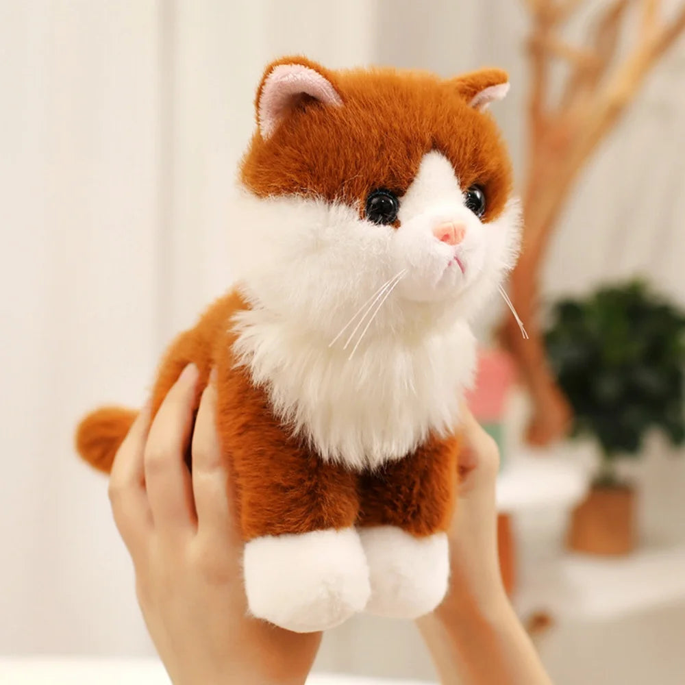 An adorable sitting kitten plush doll with orange and white fur being held by a person.