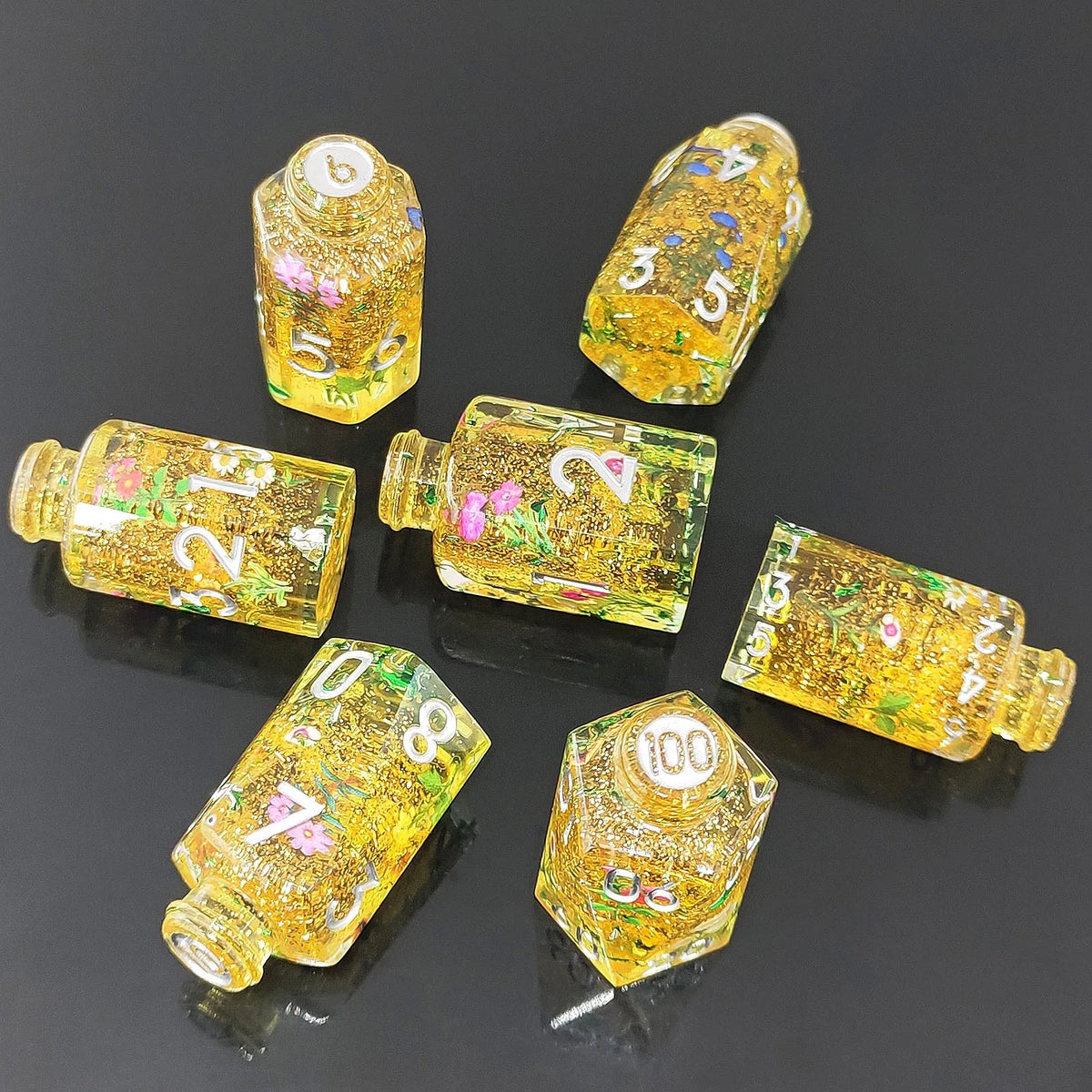 A collection of seven floral resin potion bottle polyhedral dice set in various sizes and colors.