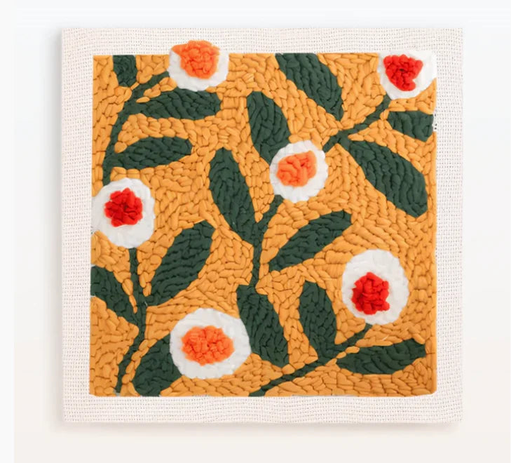A square piece of felt featuring an orange background with green leaves and white and orange flower embroidery.