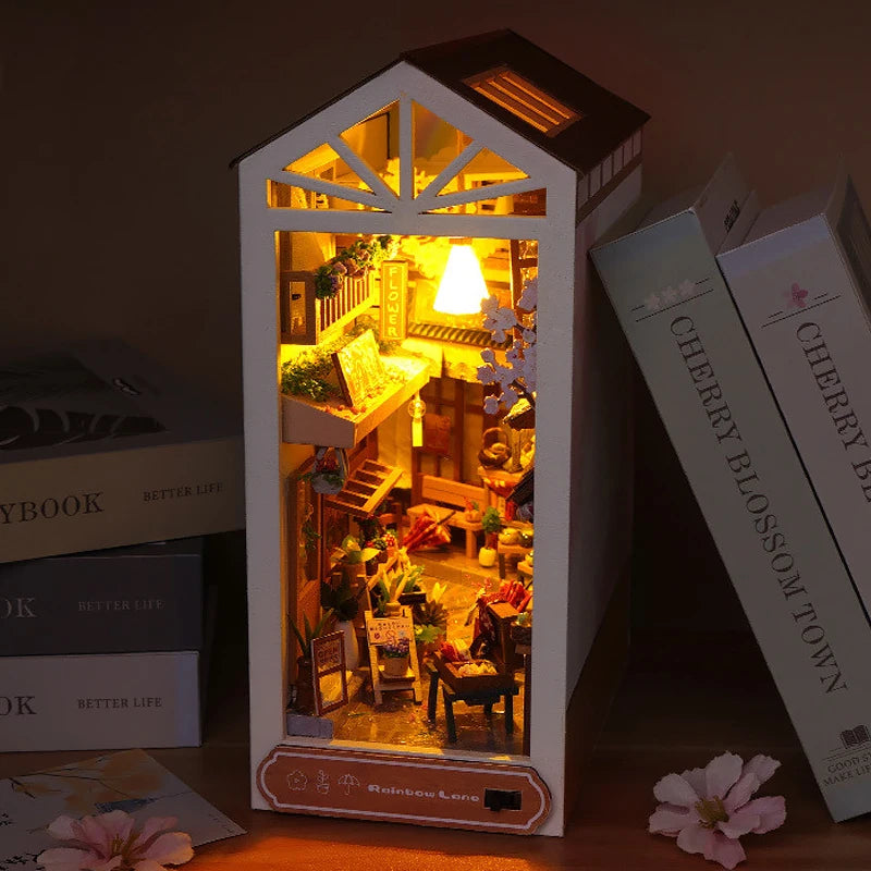 A wooden miniature bookshelf book nook kit featuring an illuminated diorama of a cozy interior scene.