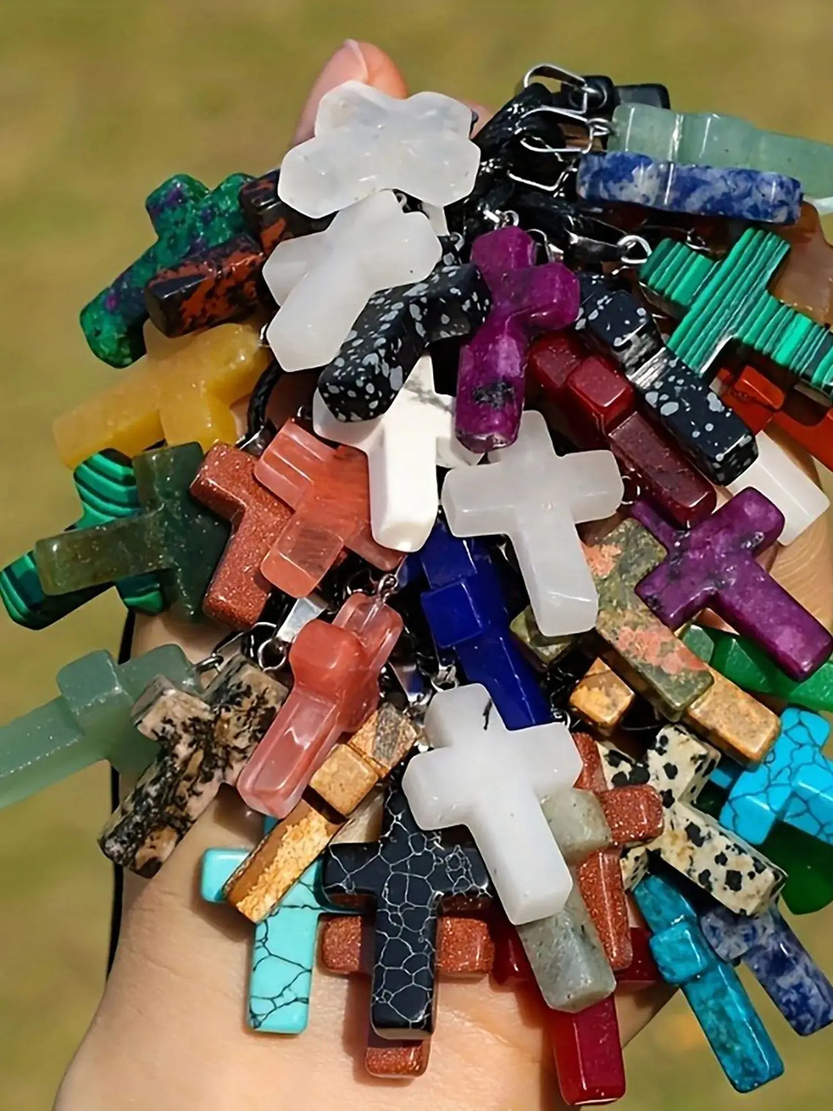 A collection of natural stone cross pendants in various colors and shapes held in a hand.