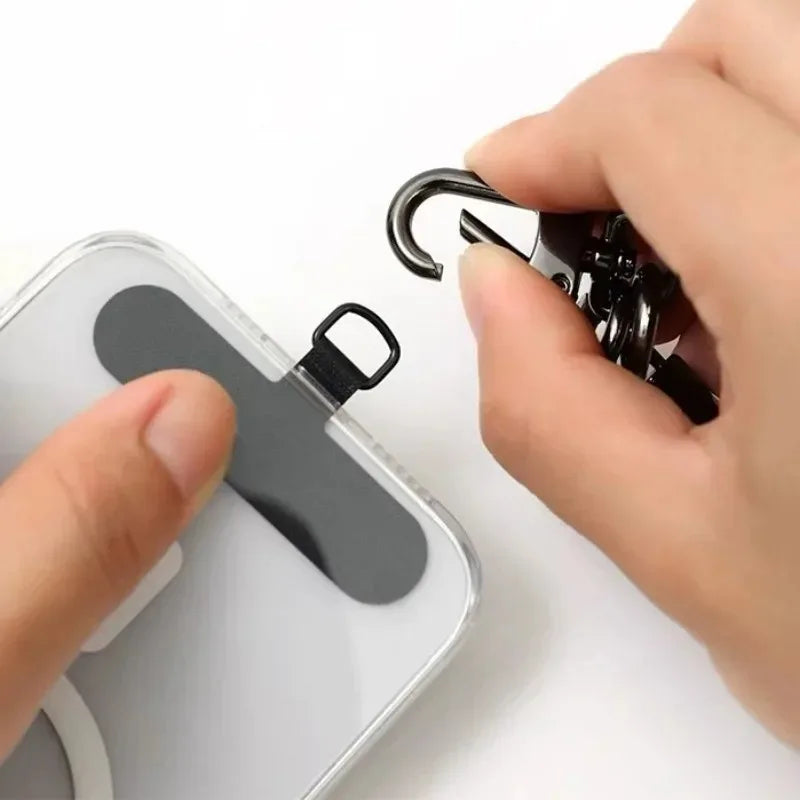 A hand is attaching a black detachable lanyard strap to the opening of a white phone case.