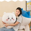 A woman is sitting on a sofa holding a white Chiikawa plush doll, with other related plush toys displayed in the background.