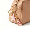 A light beige cosmetic bag with a gold chain and a pink star beaded keychain attached.