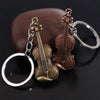 A vintage violin keychain featuring brass and copper-toned metal components resting on a dark brown surface.