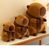 A brown plush capybara stuffed animal wearing a knit scarf sitting on a wooden surface.