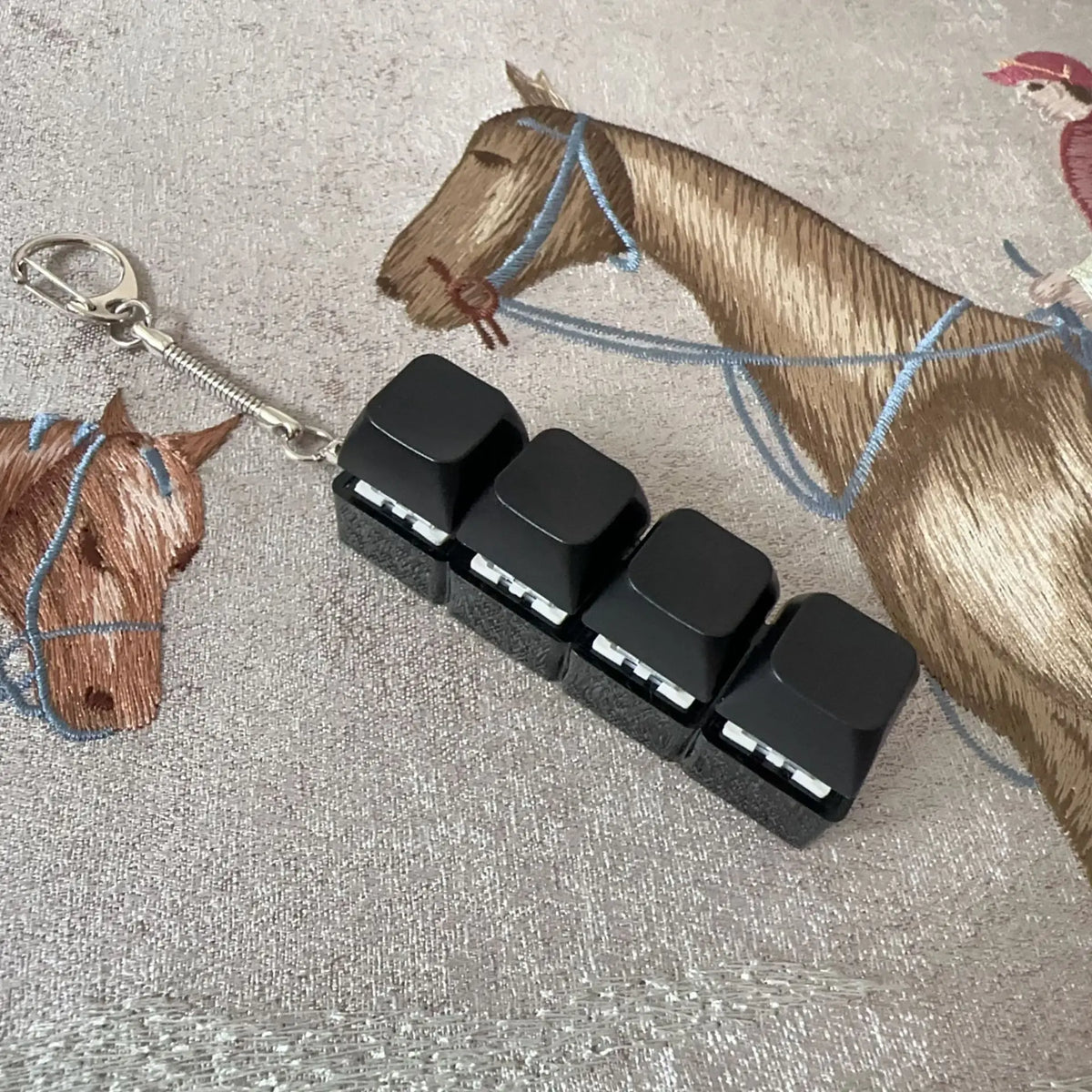 A fidget keychain featuring a horse charm and four black clicky acrylic key buttons on a silver chain.