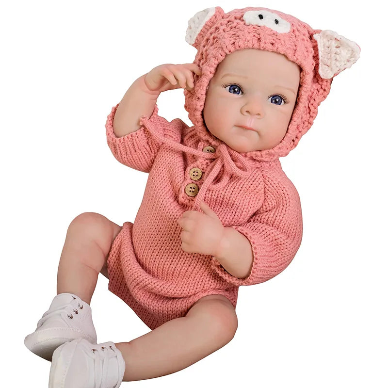 A realistic silicone reborn baby doll wearing a pink knitted hood and outfit.