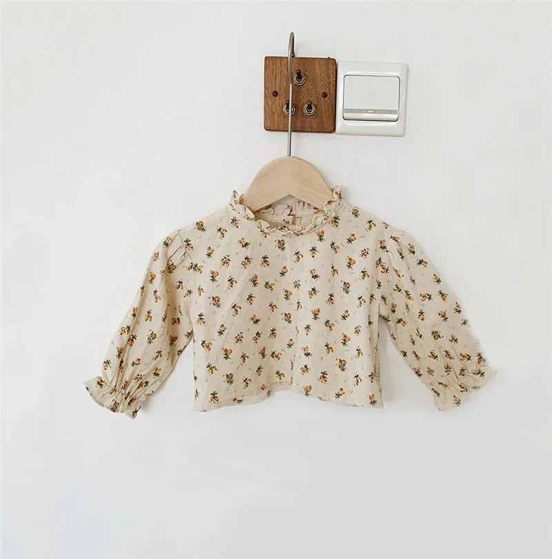 A light beige vintage floral baby girl outfit set featuring a blouse and romper, hanging on a wooden hanger.