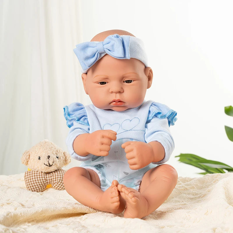A lifelike vinyl reborn doll with a blue bow and outfit sitting on a white fabric.