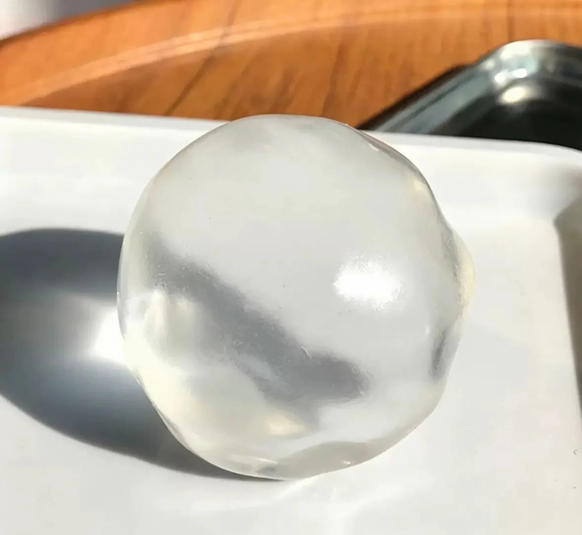 A clear, spherical stress ball with a coconut scent resting on a white plate.