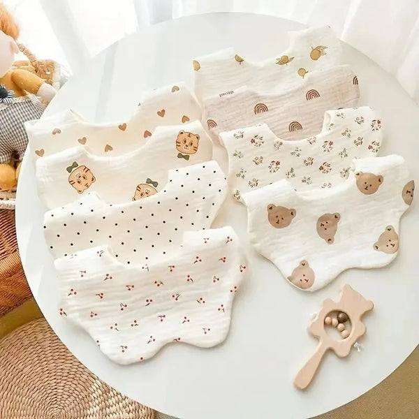 Ein Set aus drei weißen Baumwoll-Gaze-Baby-Flaschenhals-Schals mit dezenten Mustern auf einem weißen Tisch.