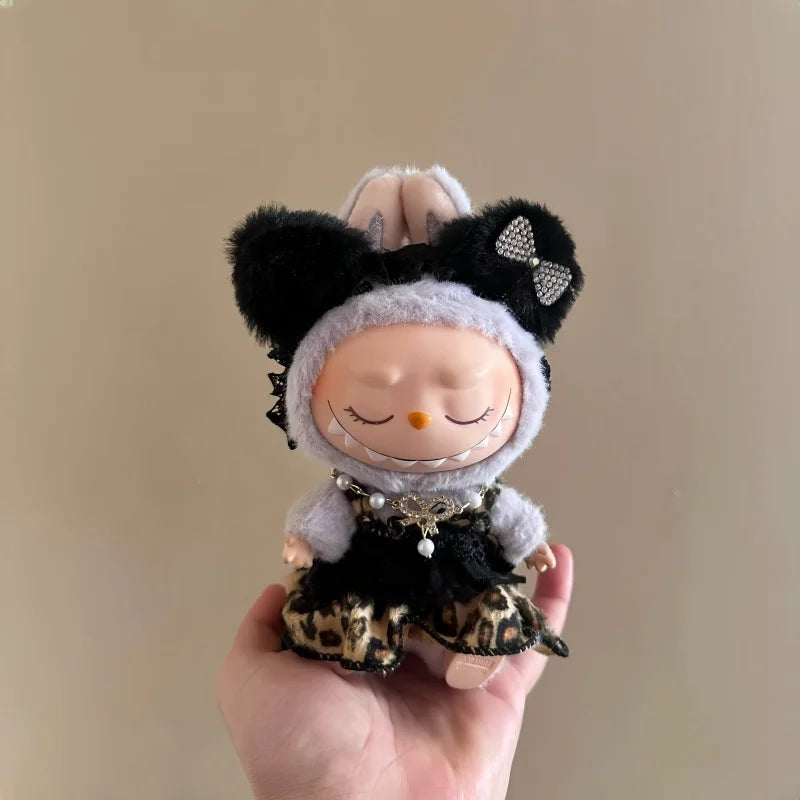 A plush doll wearing a black and white outfit with leopard print leggings is held in a person's hand.