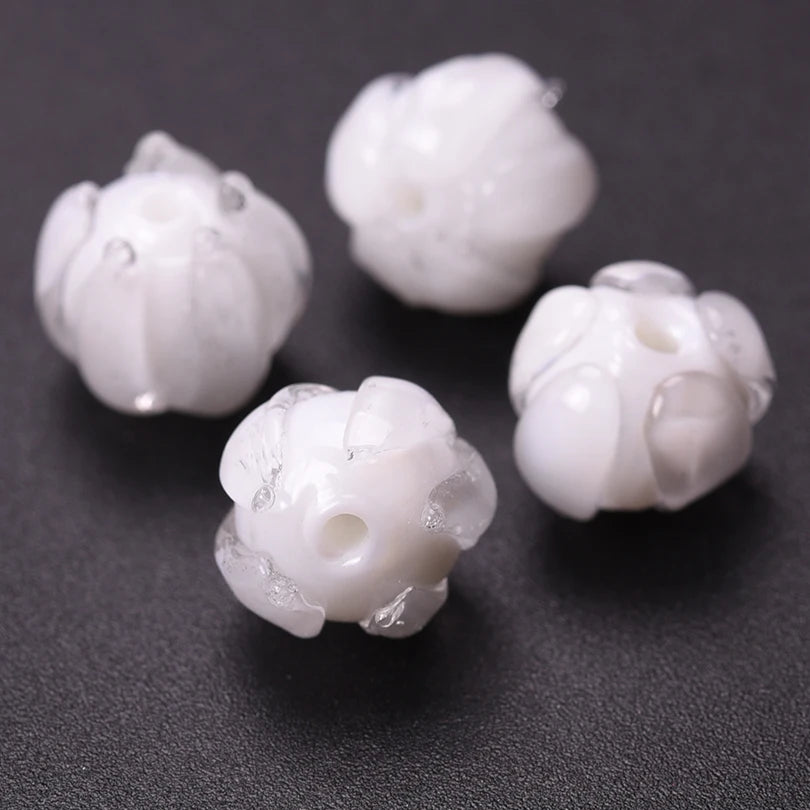 Several small, white glass charm pendants shaped like flowers are displayed on a dark surface.