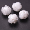 Several small, white glass charm pendants shaped like flowers are displayed on a dark surface.