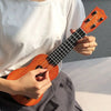 A person holds a wooden ukulele toy with adjustable tuning pegs against a light background.