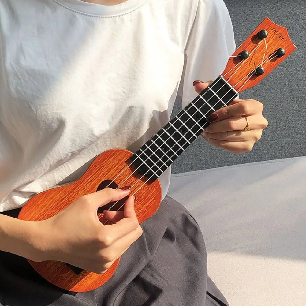 A person holds a wooden ukulele toy with adjustable tuning pegs against a light background.