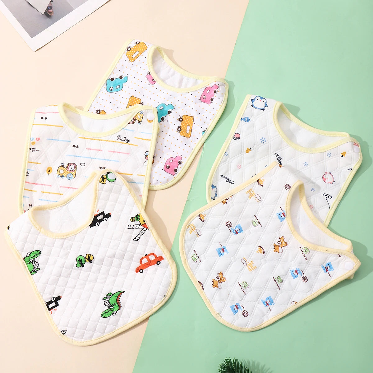 A set of three white soft cotton baby bibs with colorful embroidered designs and adjustable closures displayed on a light gre