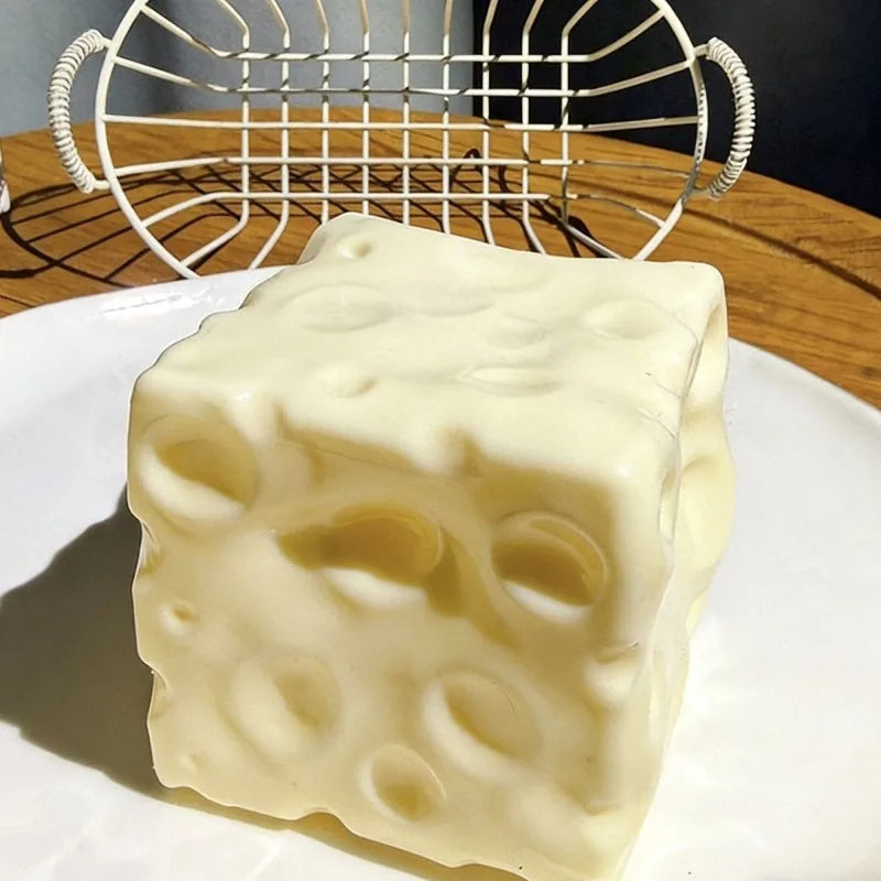 A white cheese cube stress ball with visible holes is placed on a white plate next to a wire mesh object.