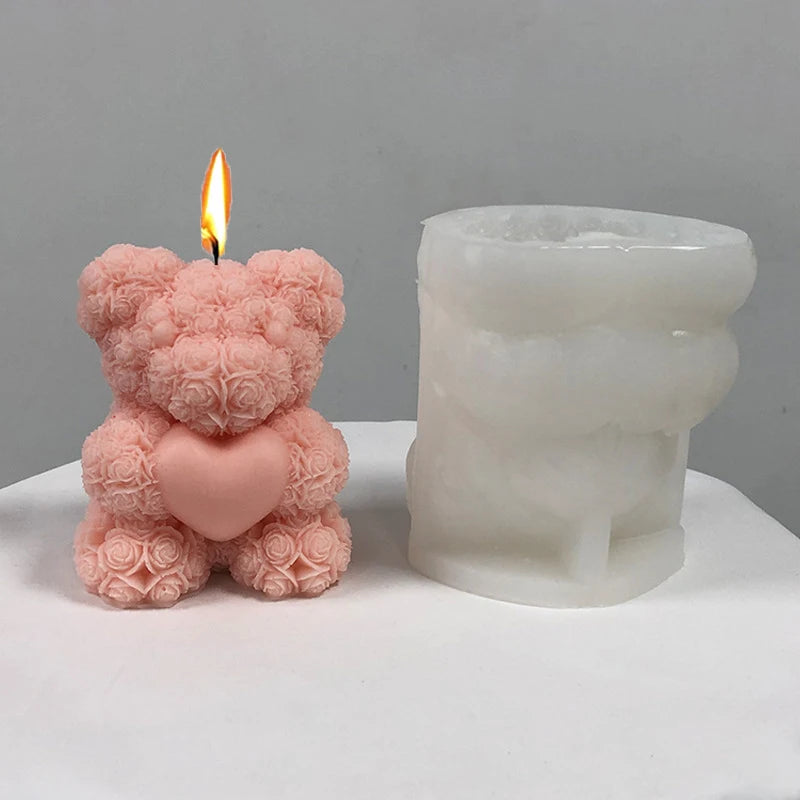 A pink silicone candle mold shaped like a bear hug, next to a lit candle.