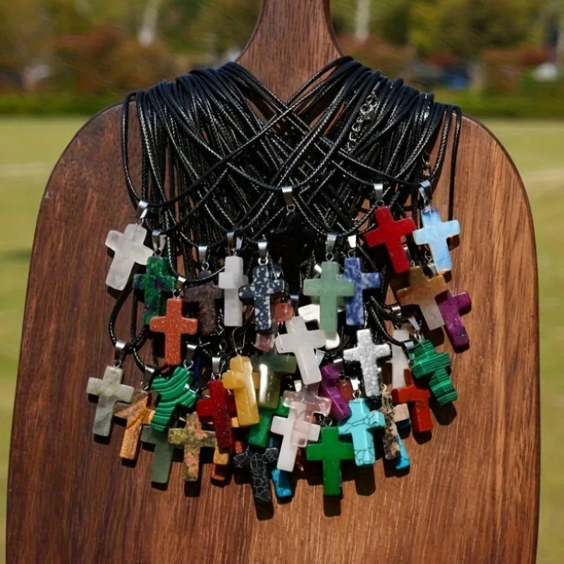 A collection of natural stone cross pendants in various colors and materials displayed on a wooden background.