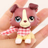 A small, brown and white miniature pet animal figure with a red and white checkered shirt accessory is held in a hand.