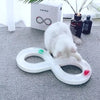 A white cat is interacting with a white, oval-shaped toy featuring colored balls on its surface.