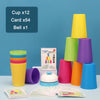 A set of colorful stacking cups, cards, and a bell for a kids game, displayed on a light blue surface.