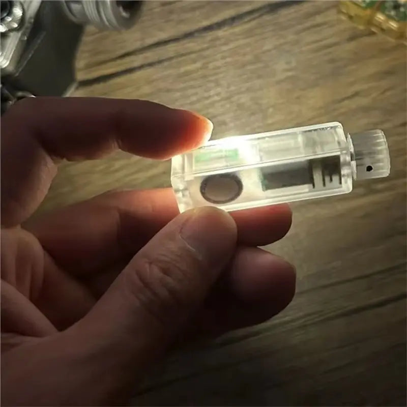 A hand holds a clear, hand-cranked fidget light bulb with an LED, demonstrating a self-powered stress relief toy.